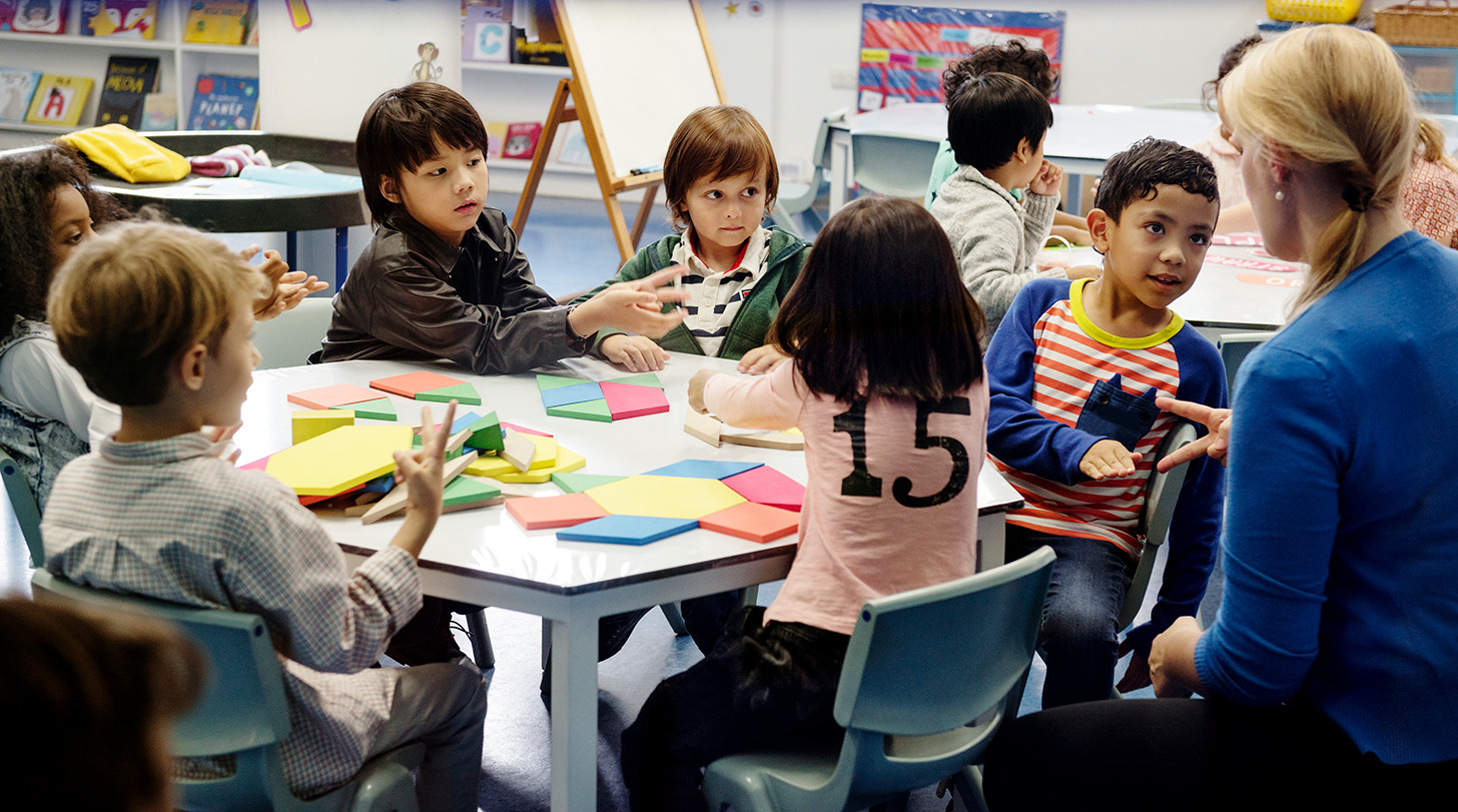 Teacher leading a small group learning activity with elementary students gathered around a classroom table.